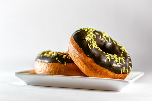 A closeup of chocolate Doughnuts with yellow sprinkles on white plate