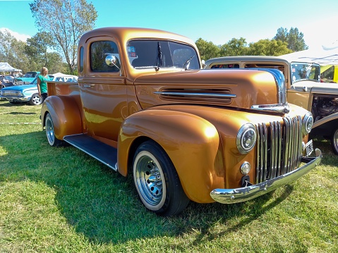 Chascomus, Argentina – April 10, 2022: Chascomus, Argentina - Apr 09, 2022: Old golden Ford custom hot rod pickup truck 1942 - 1947 in the countryside. Nature grass trees. Classic car show.