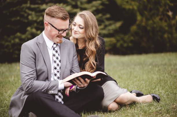 istock Romantic couple sitting on grassy lawn and lovingly reading a book 1439781383