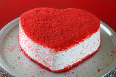 Full frame image of whole red velvet cake on cake stand for Valentine’s Day, dehydrated raspberry powder, red background, elevated view, focus on foreground