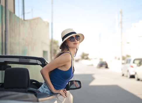 A beautiful shot of a female with a sunhat and sunglasses on a convertible sports car