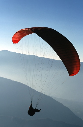 A vertical shot of a person paragliding with high mountains in the background