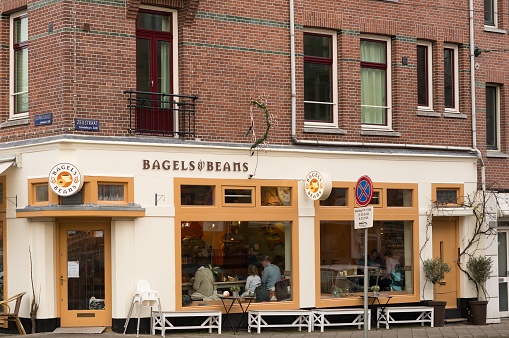 Amsterdam, Netherlands – December 23, 2016: Front entrance of a Bagels and Beans restaurant with people sitting inside in the city center.