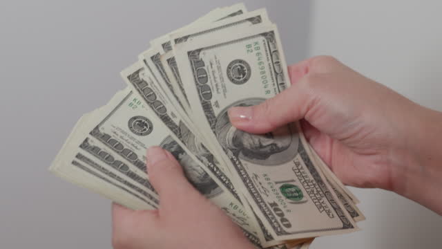 Woman converting hundred dollar bills manually at white background slow motion, The woman counts the money. Female hands counting cash us dollar banknotes. 100 us dollar bills in woman hands