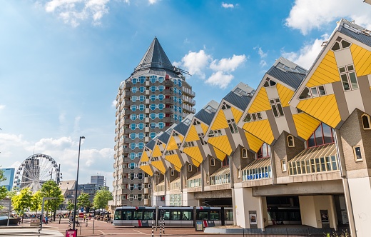 Rotterdam, Netherlands – June 22, 2019: Yellow cubic houses and pencil house in the center of Rotterdam. A bus crossing the street, some pedestrian  and the Ferris wheel in the background.