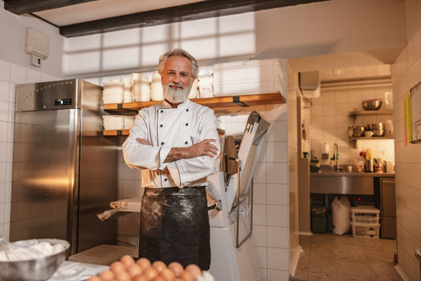 Smiley Baker With Arms Crossed Standing In The Kitchen Of The Bakery stock photo