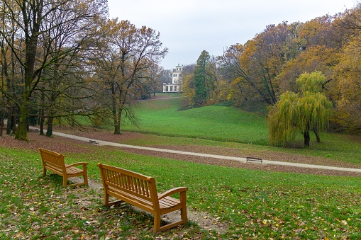 A landscape of the Maksimir Park with two wooden benches under a cloudy sky during autumn in Zagreb