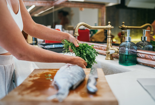 Washing the fresh green parsley herb under the kitchen sink water tap and  fish on cutting board preparing for cooking. Healthy food and fresh seafood preparation image.