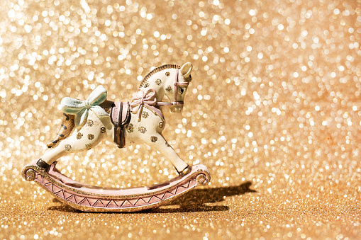 Vintage rocking horse figurine standing on a sparkling gold background. Christmas composition, space for text.