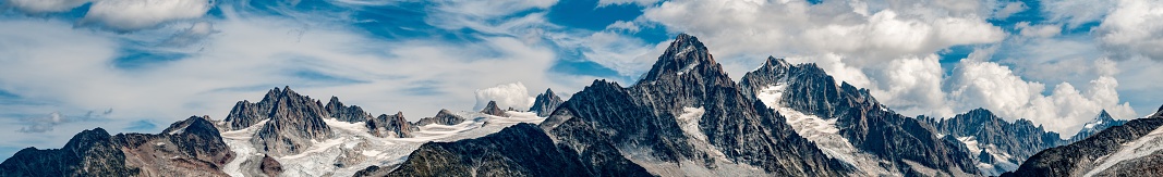 Panorama of the snow-topped Aiguille du Chardonnay, Argentiere glacier and surrounding mountains with a cloudy blue sky background from Lac Blanc