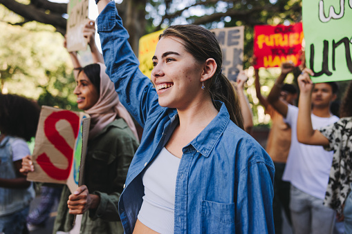 Happy young people standing up against climate change. Group of multiethnic youth activists carrying posters while marching against global warming. Diverse teenagers joining the global climate strike.