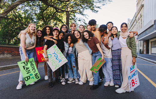 Group of diverse youth activists smiling cheerfully while standing together at a climate change protest. Multicultural young people joining the global climate strike.