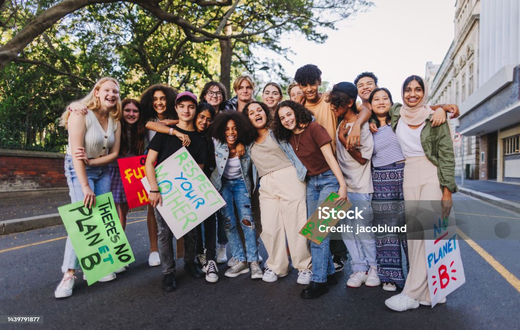Diverse youth activists holding a climate change protest Group of diverse youth activists smiling cheerfully while standing together at a climate change protest. Multicultural young people joining the global climate strike. Activist Stock Photo