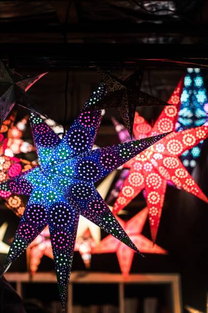 istock Vertical closeup shot of illuminated colorful star-shaped decorations outside on blurred background 1439791966