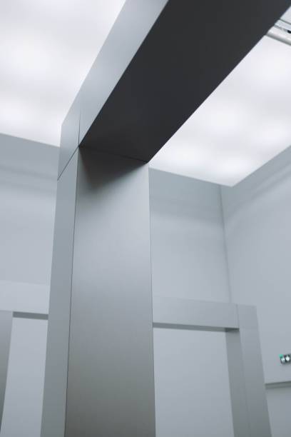 istock Low angle view of a corner of a silver ceiling under white lamp lights surrounded by grey walls 1439792536