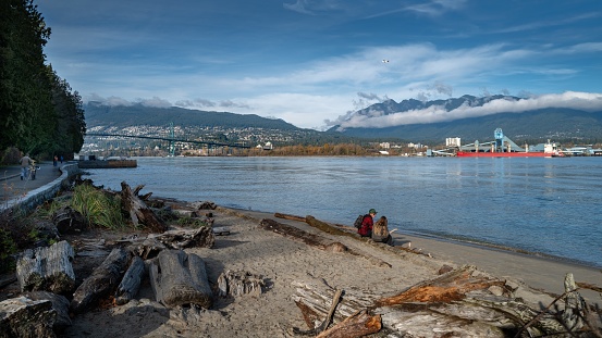 Vancouver, Canada – November 13, 2019: The people sitting near the lake in the Seawall of Stanley Park in Vancouver with the Lions Gate Bridge in the background towards North Vancouver