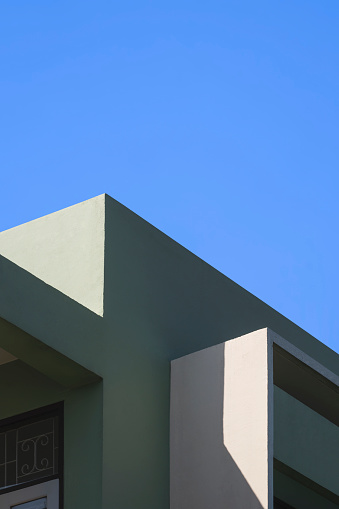 Sunlight and shadow on surface of shading fin concrete on green and beige house building wall against blue clear sky in vertical frame