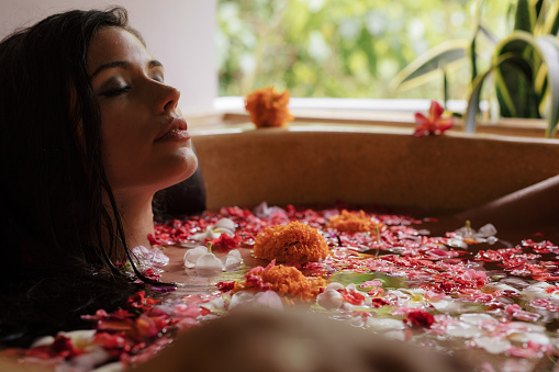 Shot of beautiful young woman relaxing in bathtub with flower petals. Female having flower bath at a spa.