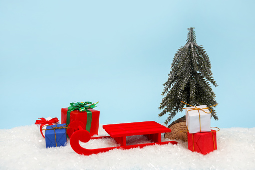Podium in the form of a sled for the presentation of your product on a blue Christmas background with snow, gift boxes and christmas tree. copy space