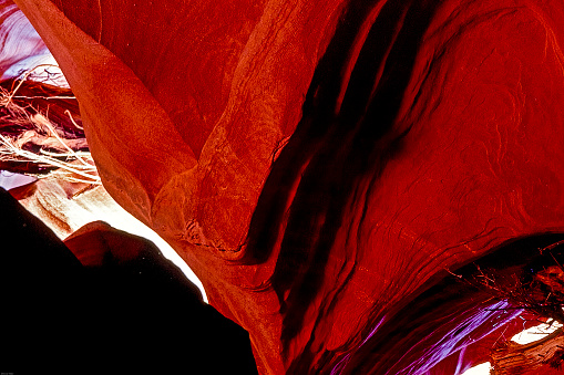 Red slick rocks unfold in an accordion shape to form an abstract background with light coming in through a crack.