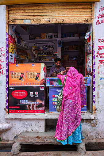 Pushkar, India - November 7, 2019: Street electronic shop vendor tops up recharges woman mobile phone in street of Pushkar, Rajasthan, India