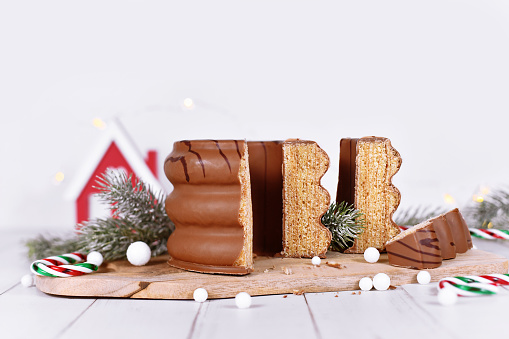 Cut open traditional German layered winter cake called 'Baumkuchen' glazed with chocolate in front of seasonal decoration