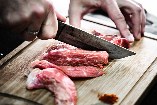 Butcher cutting beef meat on a wooden table on the dark background