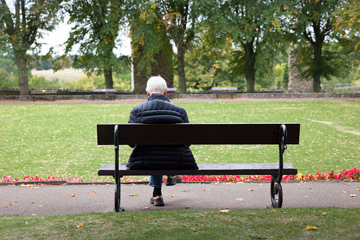 Knaresborough, UK - September 20, 2022. Older man with grey hair sitting alone on a park bench in autumn. Knaresborough, Yorkshire, UK