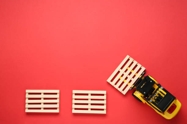 istock Toy forklift and wooden pallets on red background, flat lay. Space for text 1439801543