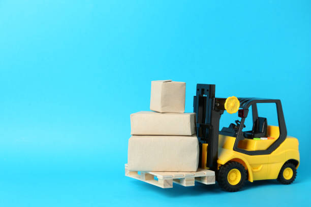 istock Toy forklift with wooden pallet and boxes on light blue background, space for text 1439801599