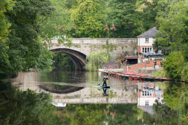 Knaresborough, UK - September 20, 2022. Man in a wetsuit kneeling on a paddle board on the River Nidd, Knaresborough, North Yorkshire, UK