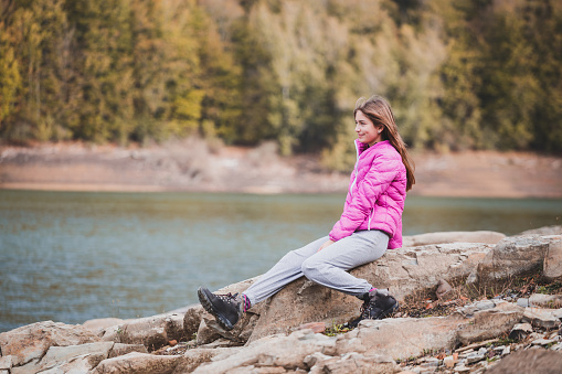 Young girl sitting on rocks near a lake shore and beautiful forest in background. Irati forest, navarre, Spain. Active lifestyle concept.