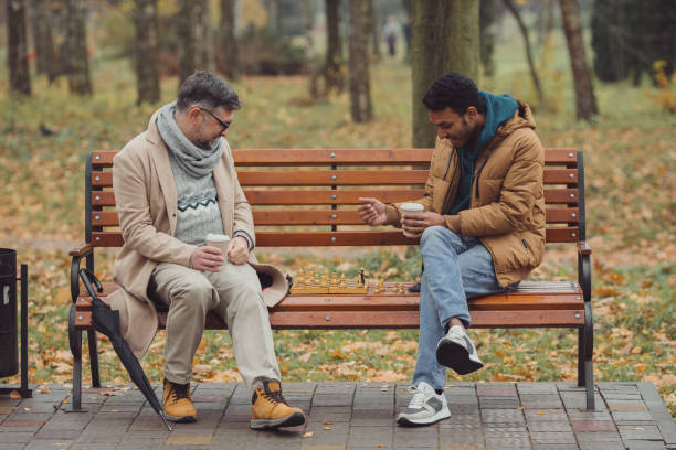 istock Multi-ethnic men, teacher and student playing chess in autumn park on a bench. 1439802223