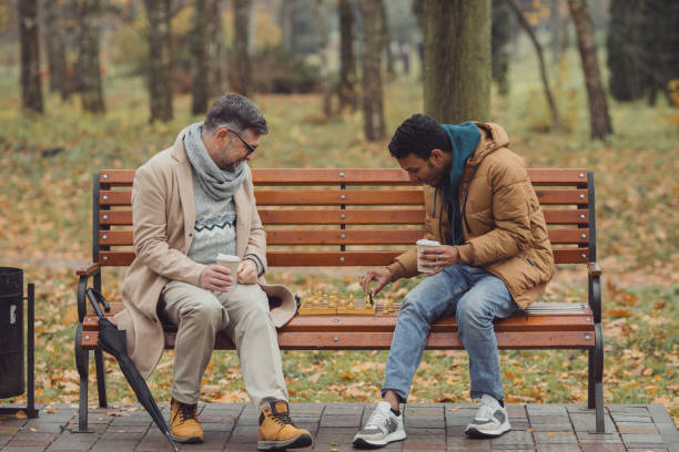 istock Multi-ethnic men, teacher and student playing chess in autumn park on a bench. 1439802228