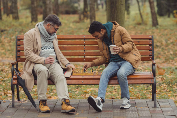 istock Multi-ethnic men, teacher and student playing chess in autumn park on a bench. 1439802229