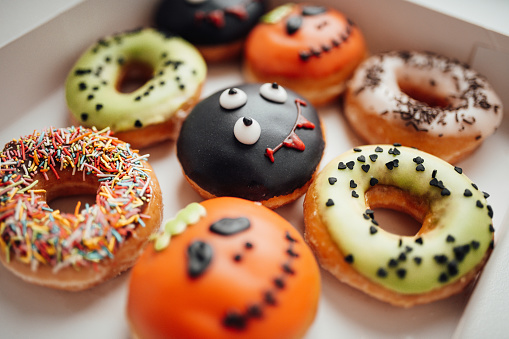 Donuts with Halloween decoration of monsters with spooky face and zombie by syringe with sugar syrup. Different colorful traditional sweets and doughnuts of hallows eve at autumn season indoor