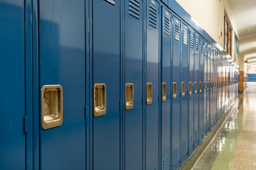 Foto de un casillero de metal azul a lo largo de un pasillo anodino en una típica escuela secundaria de los Estados Unidos. No hay información identificable incluida y nadie en el pasillo. photo