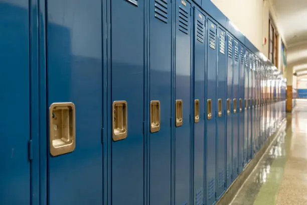 Photo of a blue metal lockers along a nondescript hallway in a typical US High School. No identifiable information included and nobody in the hall.