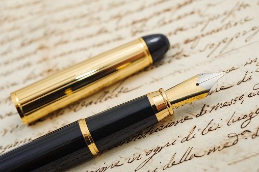 Antique desktop surface with old books, pen kit and blank parchment with quill pen in inkwell. Same series: