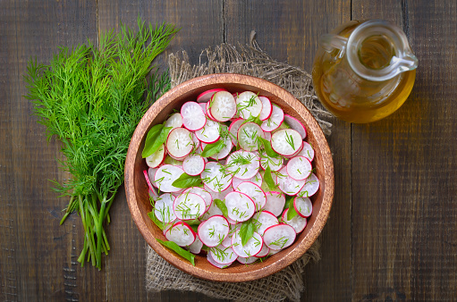 Radish salad in bowl and fresh dill on wooden table. Top view, flat lay