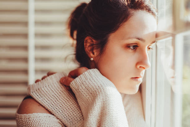 istock Depressed woman looking through window 1439806560