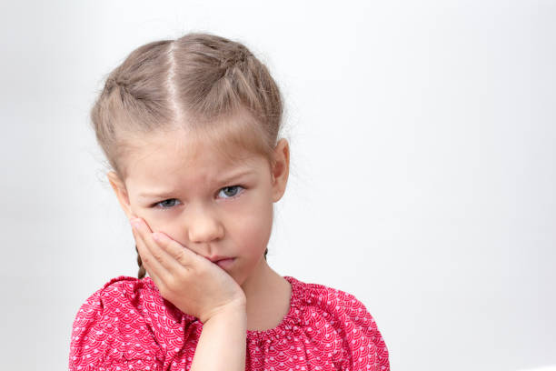 istock Serious child holding hand on cheek feeling ache 1439808668