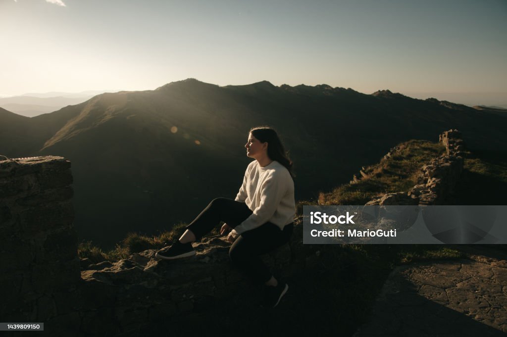 Young woman contemplating a beautiful mountain area A young woman sitting and contemplating a beautiful mountain area at sunset Cantabria Stock Photo