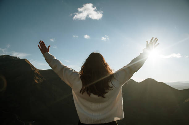 istock Young woman with arms raised by mountains at sunset 1439809151