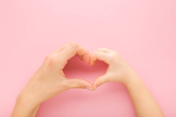 istock Heart shape created from little daughter and young mother hands on light pink table background. Pastel color. Lovely emotional, sentimental moment. Love, happiness and safety concept. Top down view. 1439810023