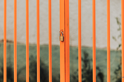 Orange closed metallic gate with bars and a padlock as the entrance or access to a home