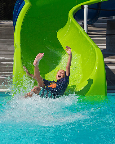 Boy joyfully entering swimming pool from green water slide