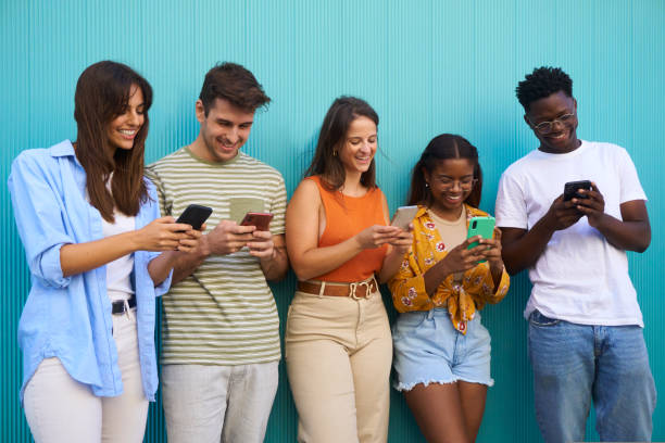 istock Group of mixed race young people using mobile phone outdoor. Students isolated in blue background. 1439811236