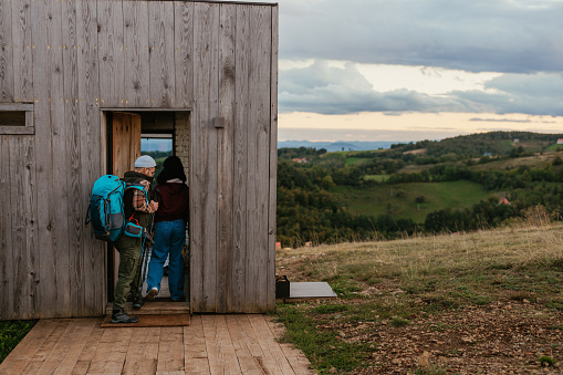 Two young hikers are entering their mountain cabin after a day of hiking.