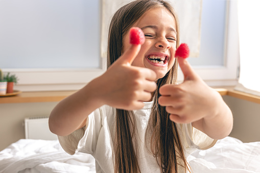 Funny little girl with raspberries on her fingers sits in bed in the morning, the concept of health and vitamins.